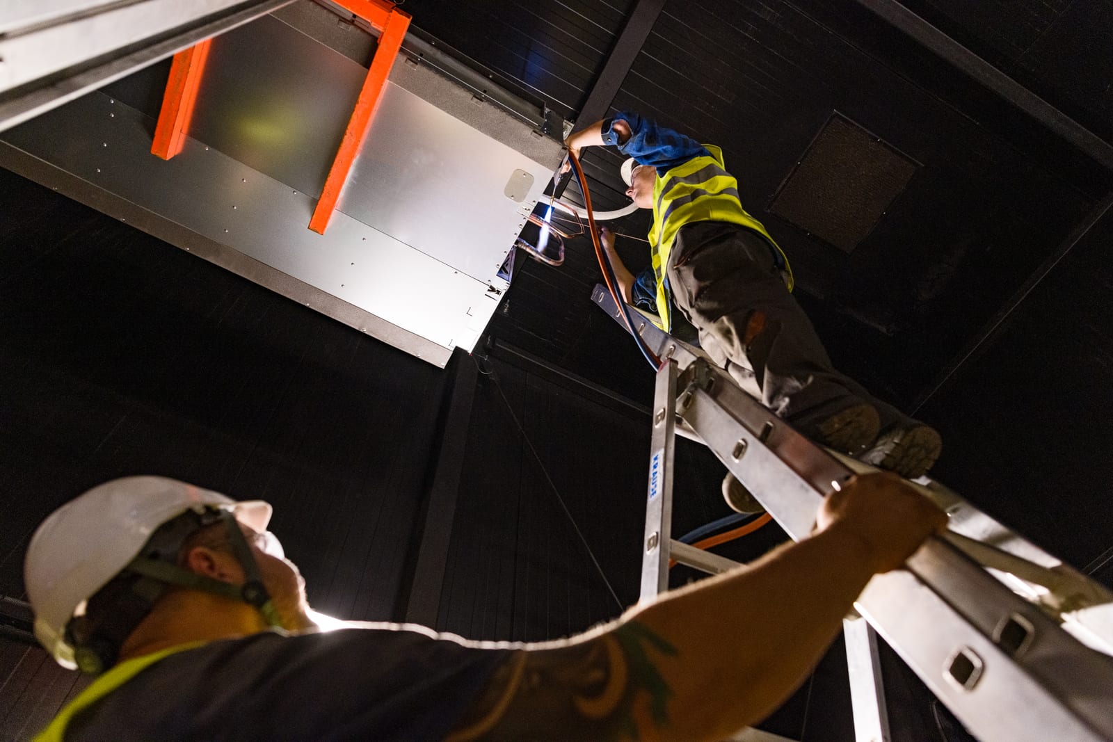 Serwisanci Clima Line pracują na drabinie przy instalacji pod stropem hali