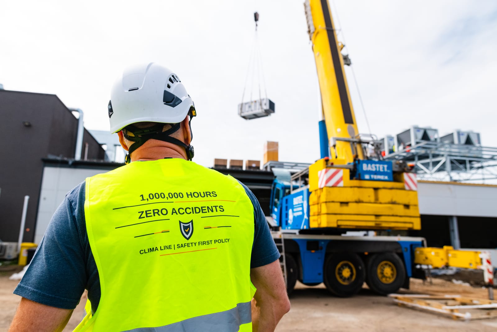 A Clima Line employee in a vest printed with the health and safety policy watching a crane lift an air handling unit